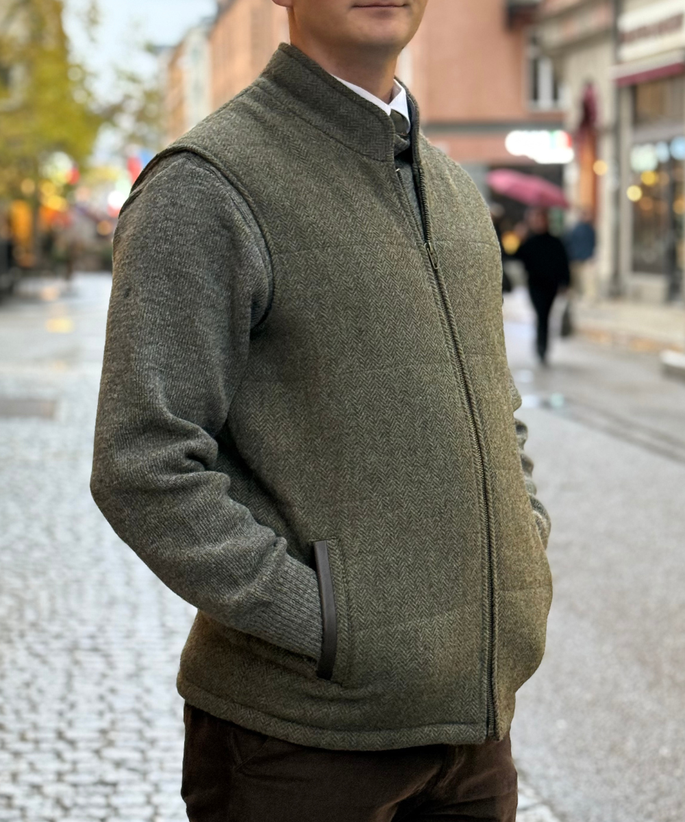 Grön body warmer i tweed med fiskbensmönster, dragkedja och läderdetaljer på fickorna för herr – Celtia Stockholm